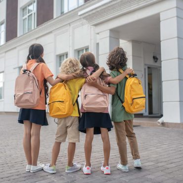 Near school building. Schoolchildren standing in school yard and looking at school building